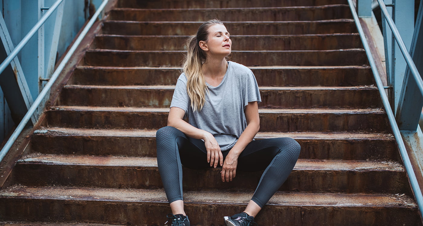 a woman sitting on stairs catching her breath after exercising